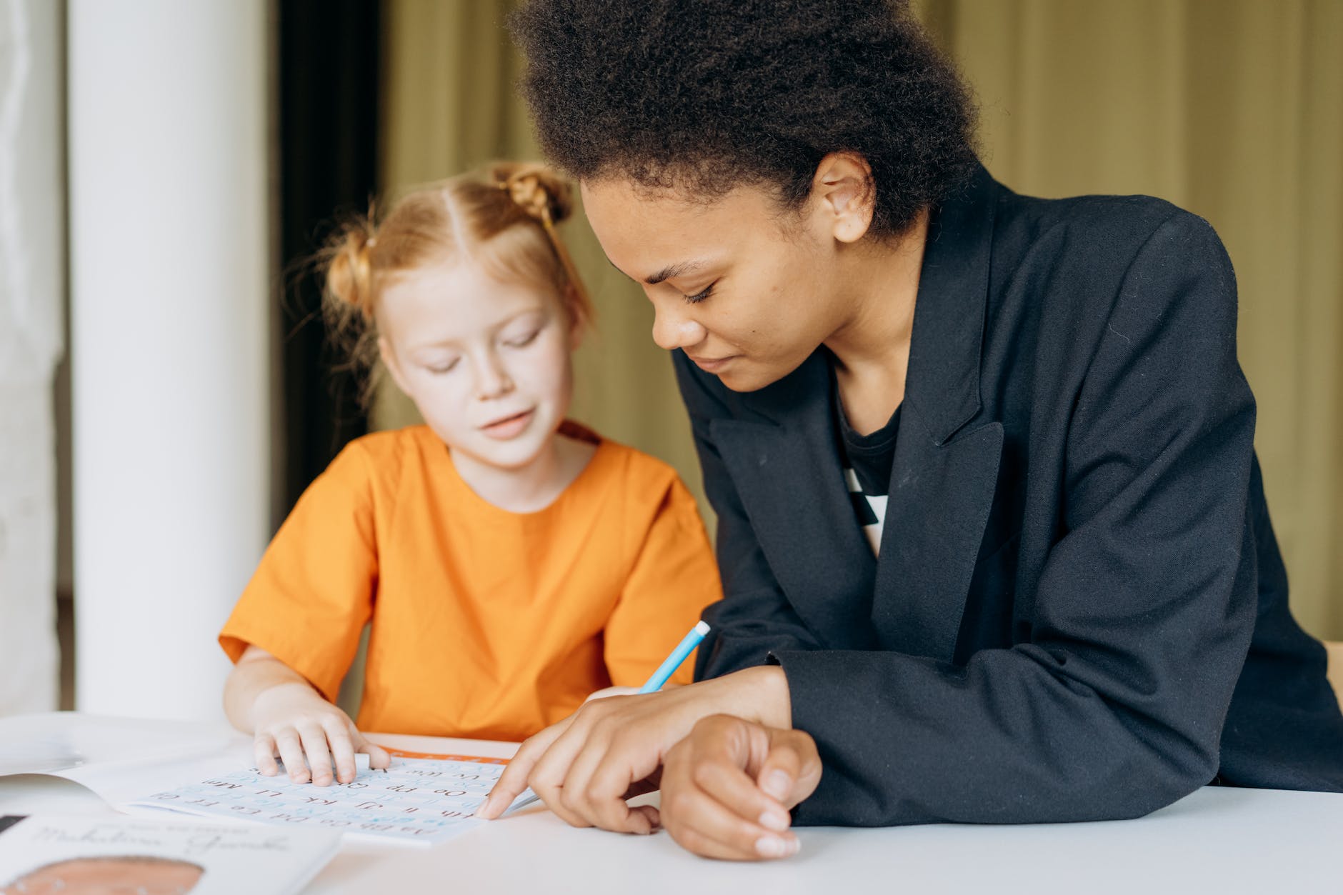 Black woman wearing suit helping red haired student with writing letters
