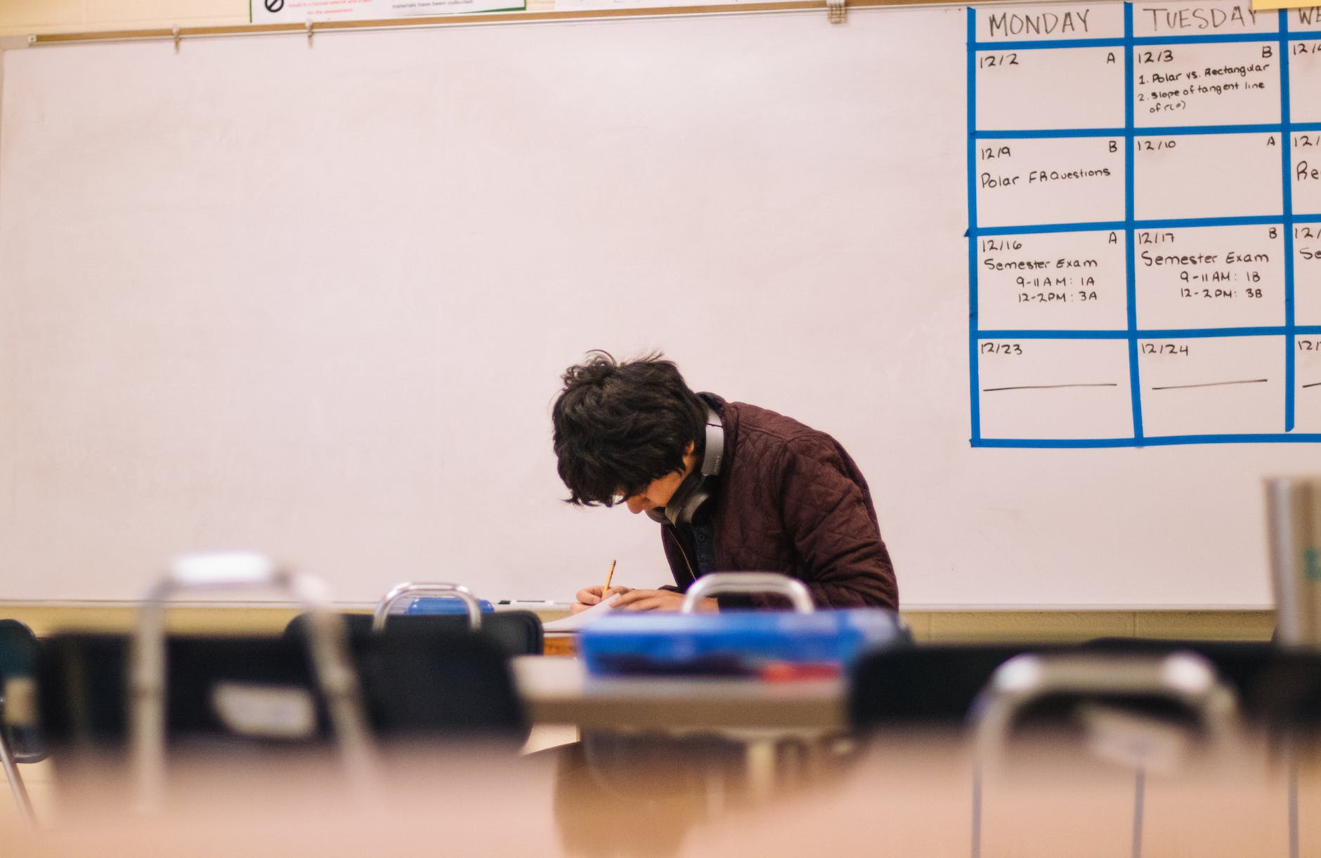 student taking exam in empty classroom with headphones and head down while they hold a pencil and paper