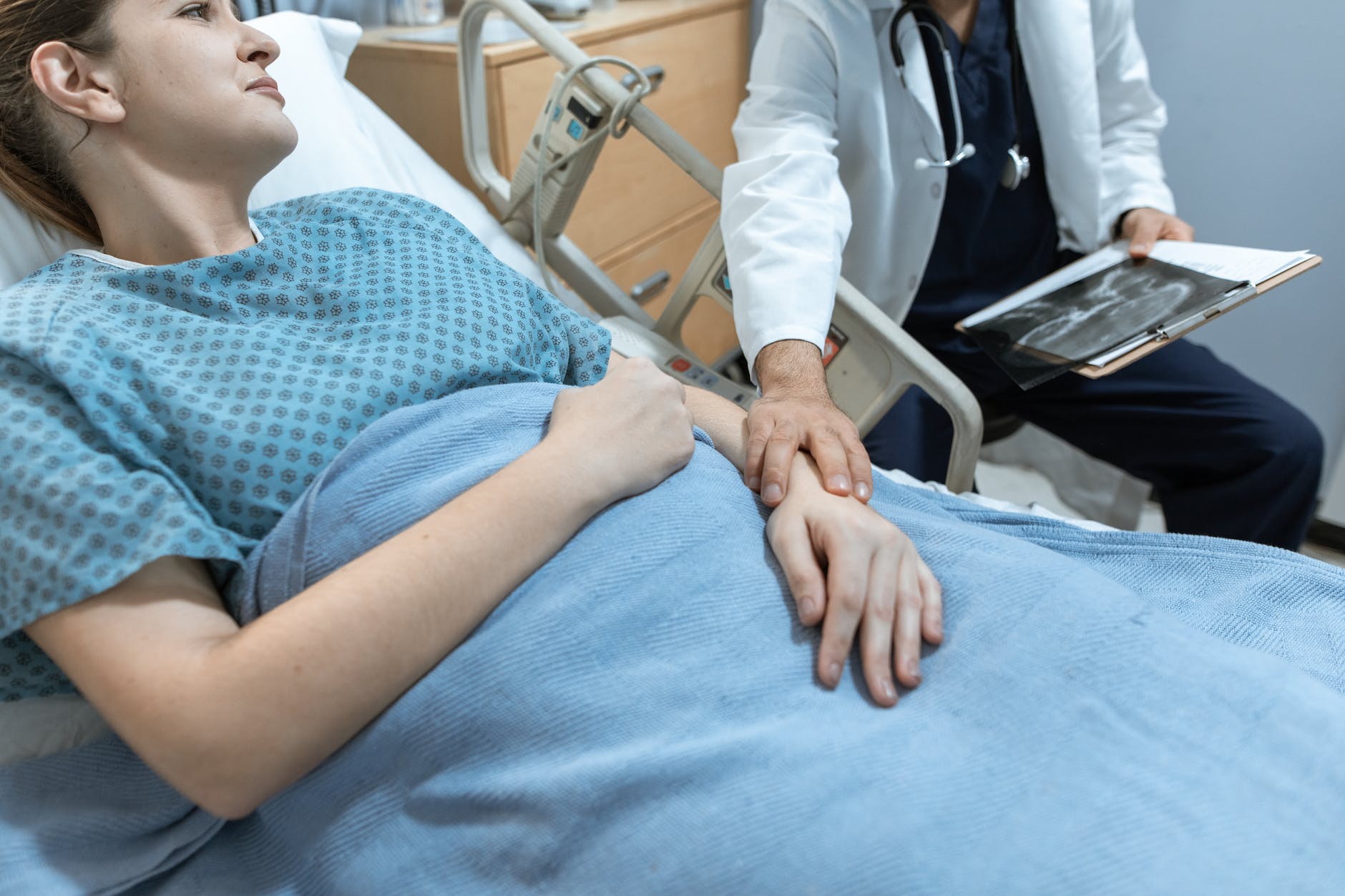 patient in hospital bed and hand of person wearing medical white coat holding hand of patient