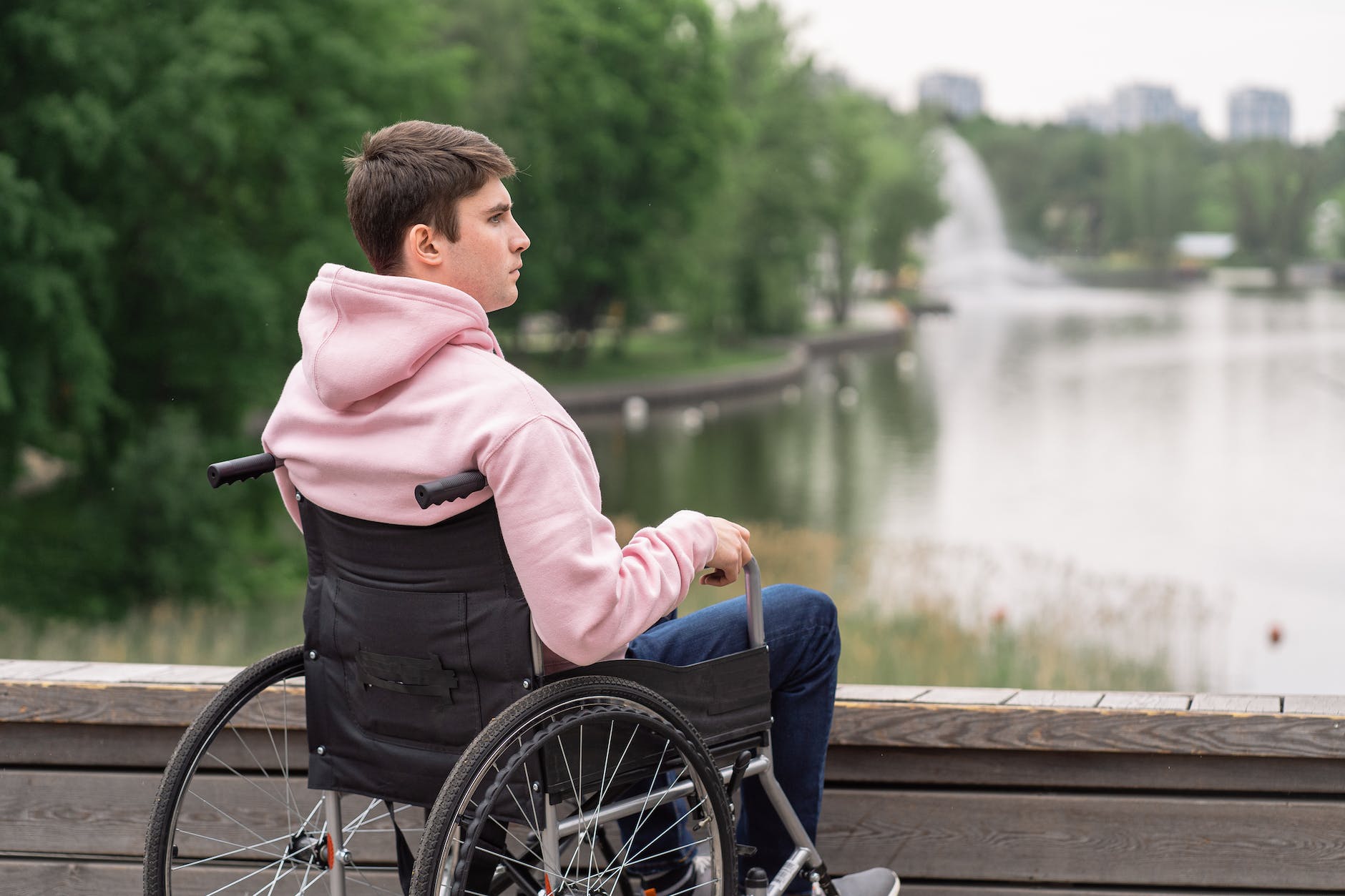Man sitting oin. wheelchair watching water in pond or lake.