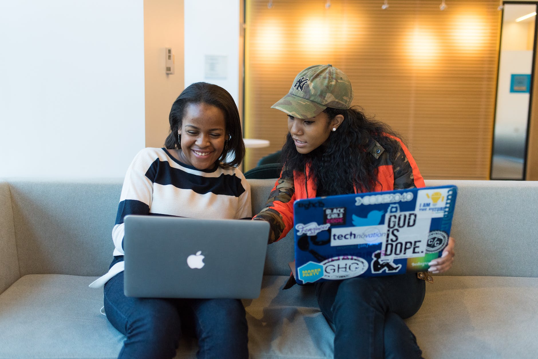 two black women working on laptops on couch.