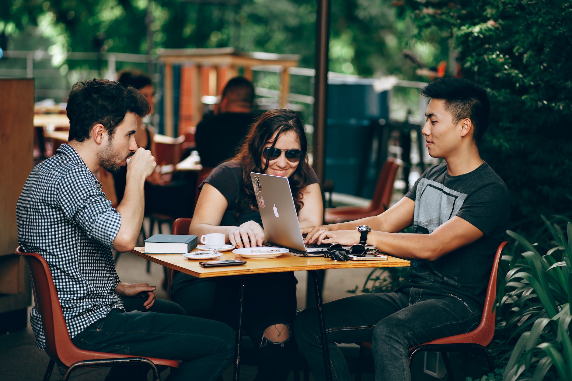 college students at outside table working on laptop. Three people around table.