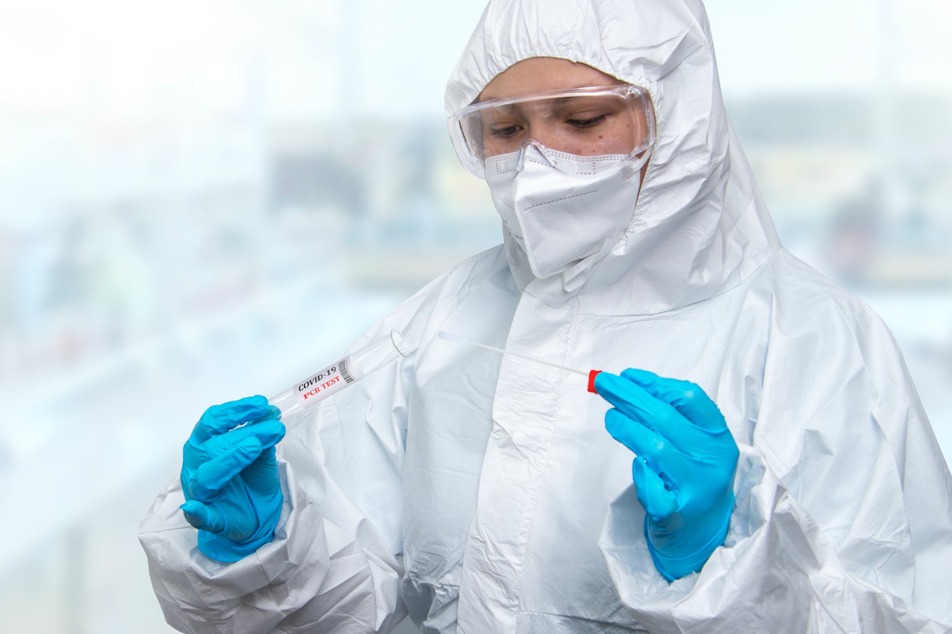 A person wearing personal protective equipment and holding a test swab and conical tube