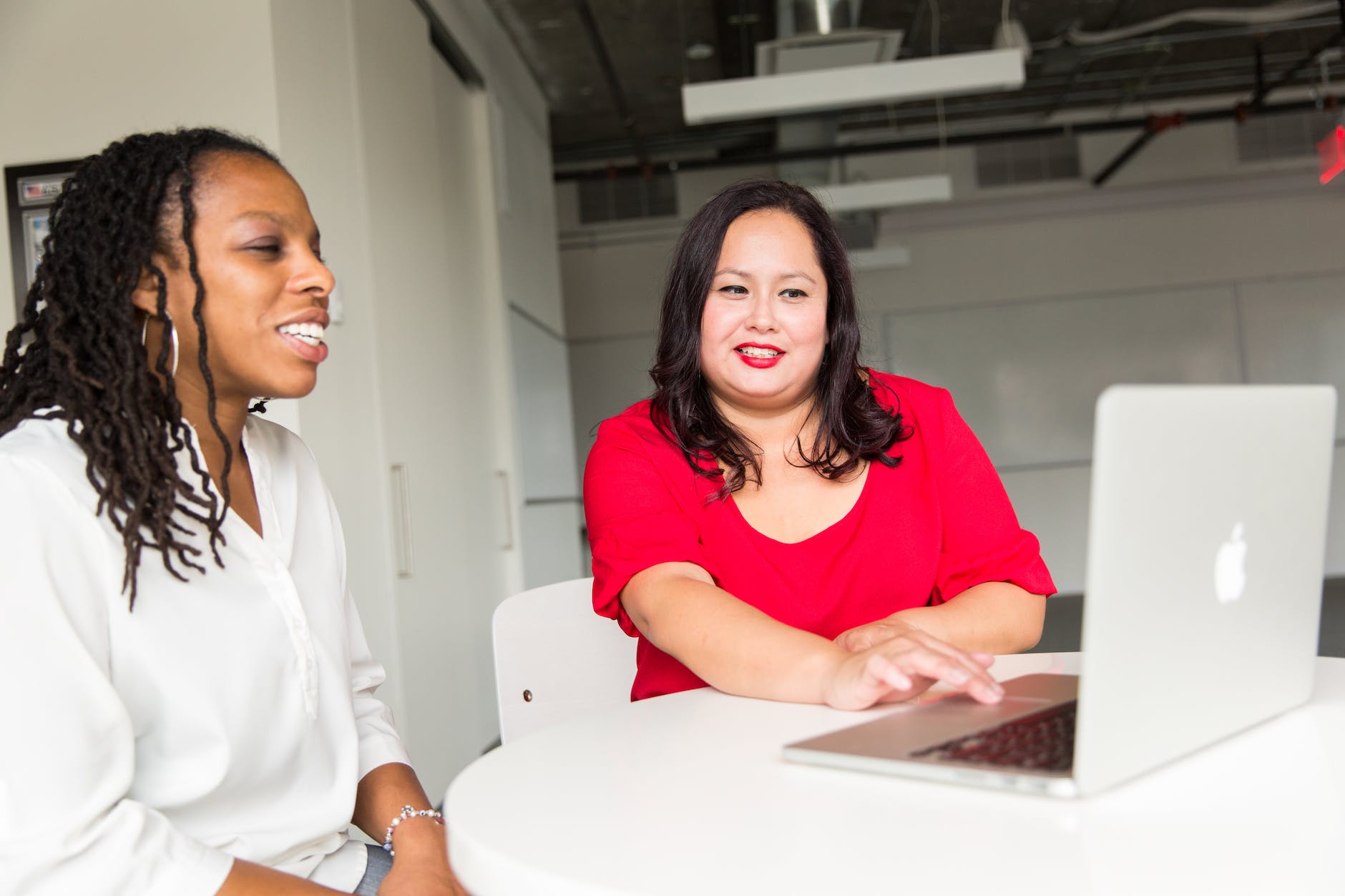 Woman wearing red top holding silver Macbook and working with another female 