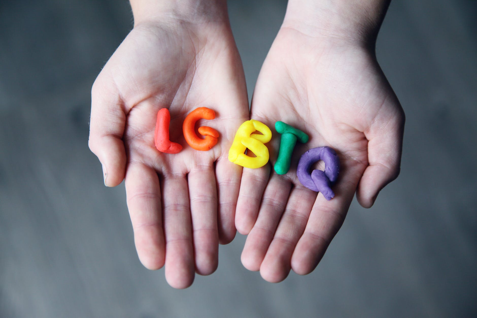 open palms holding LGBTQ letters in red, orange, yellow, green and purple