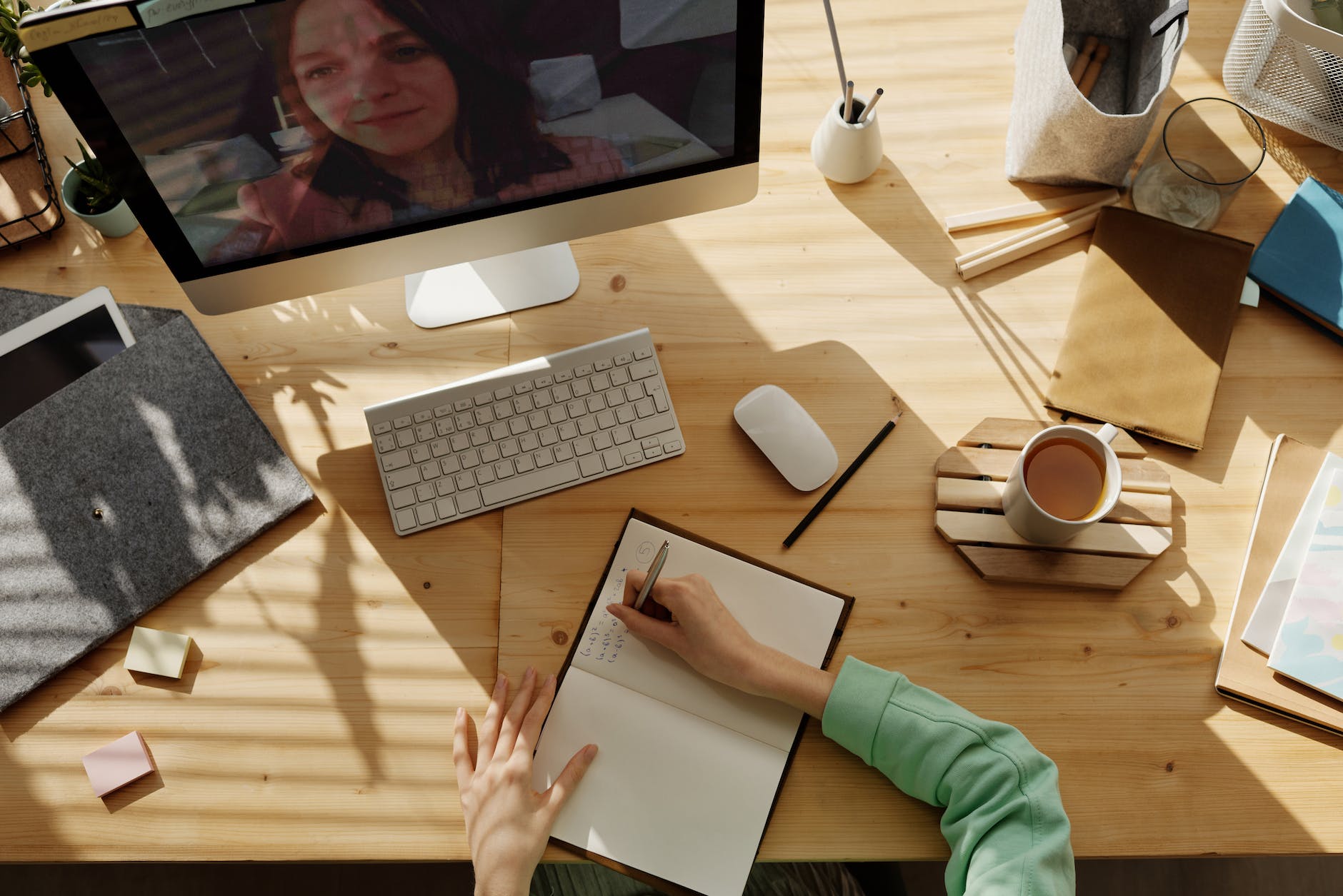 person writing in notebook in front of desktop