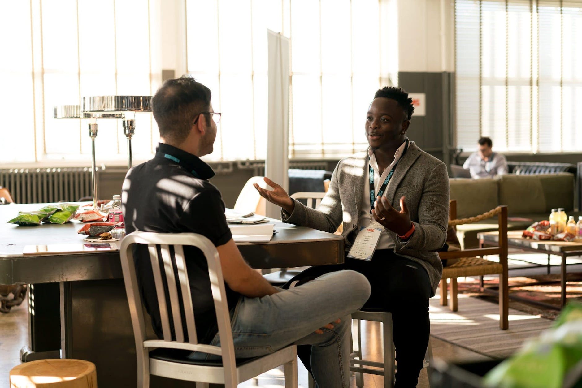 Black man having a conversation with another person in a room with tables and couches
