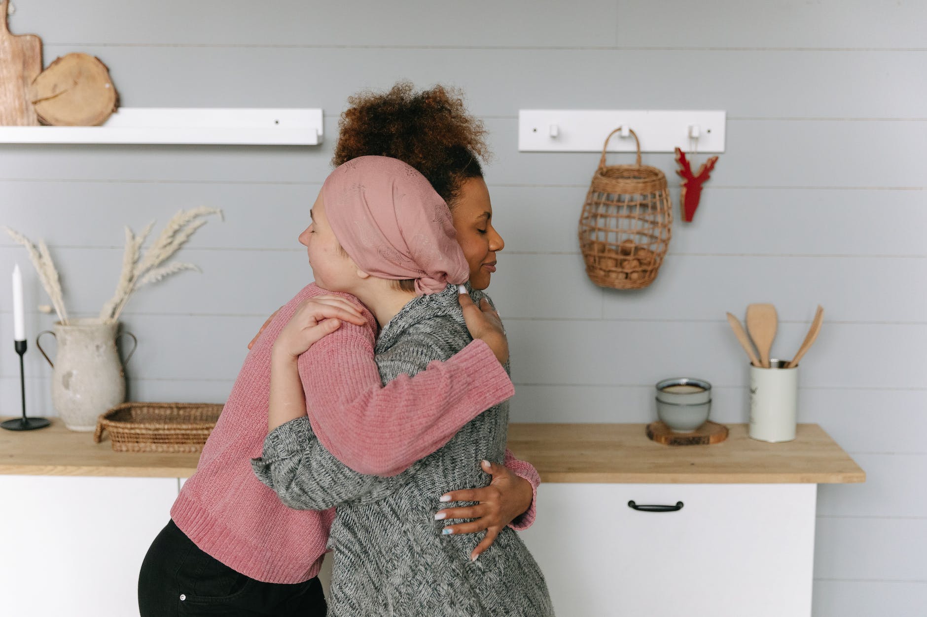two women embracing. A white woman has a head scarf. A black woman is hugging her.