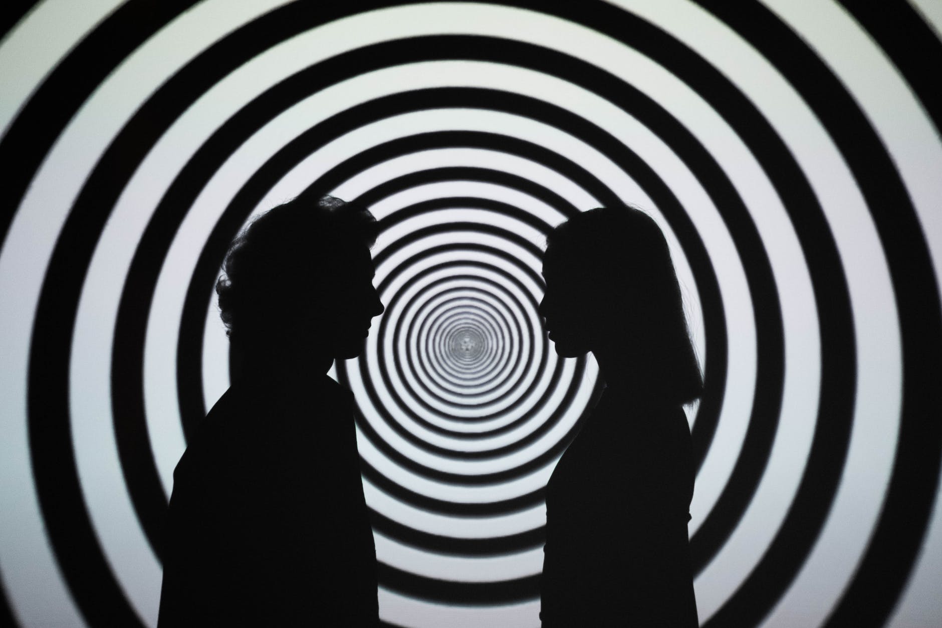 Silhouette of two people standing in front of white and black striped wall.