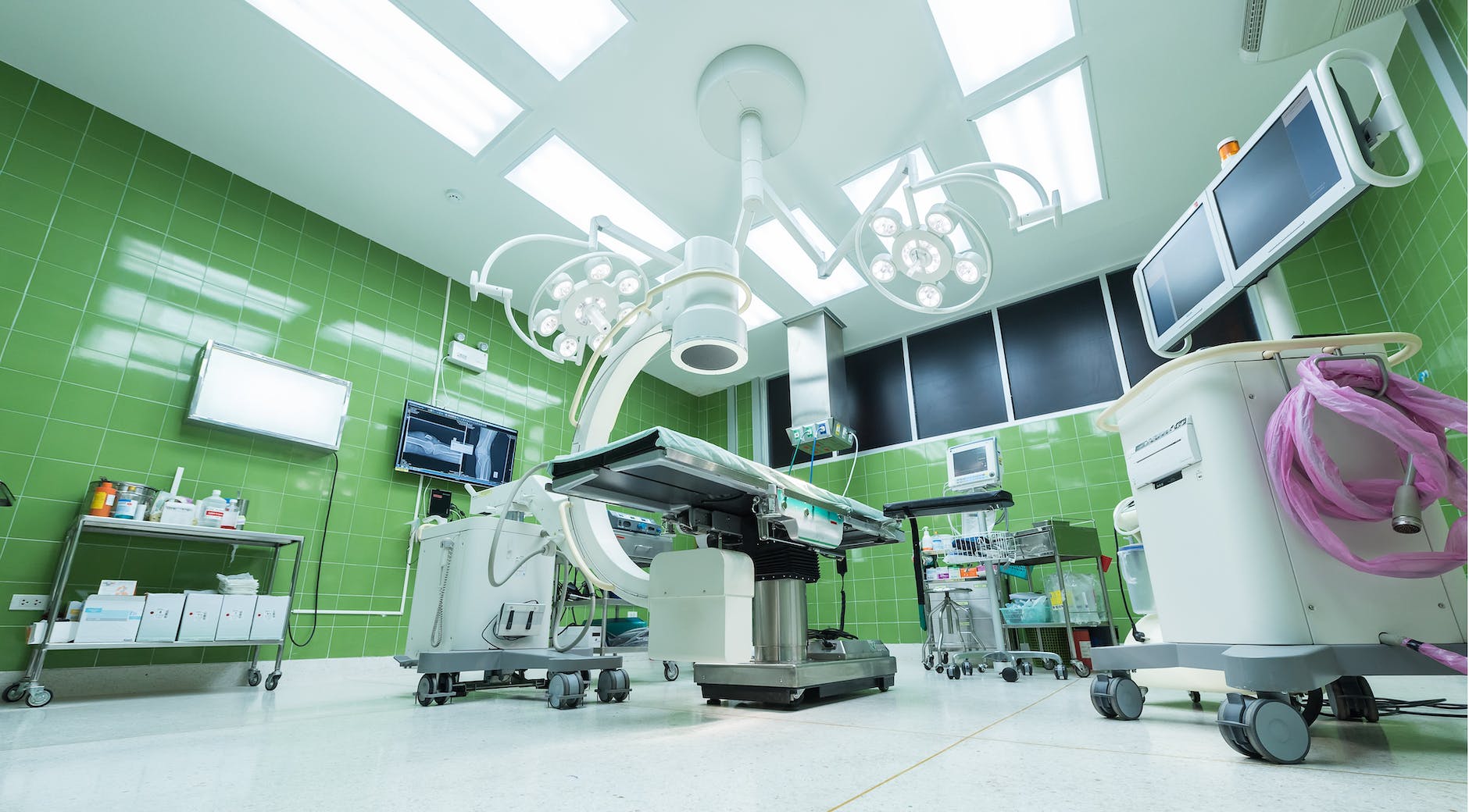 view of operating room with green tiles on the walls, white floor, and several pieces of equipment