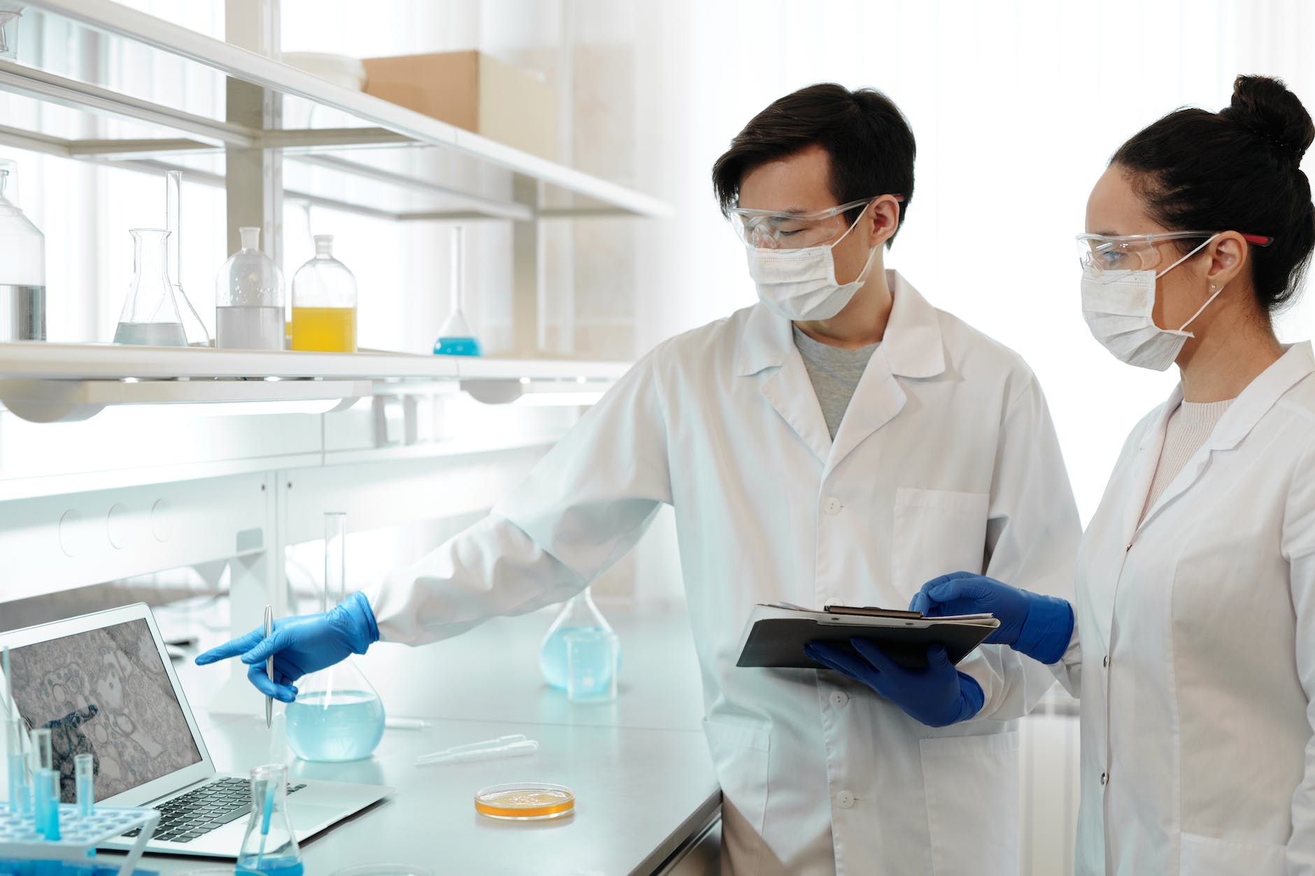 two scientists working inside the laboratory. One is pointing to laptop screen.
