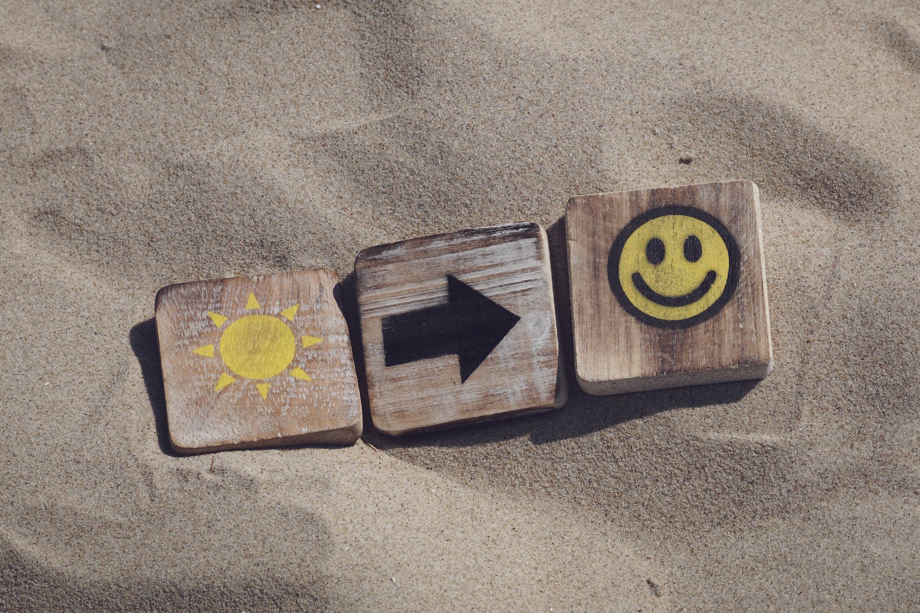 three brown tiles on sand with sun, black arrow, and smiley face