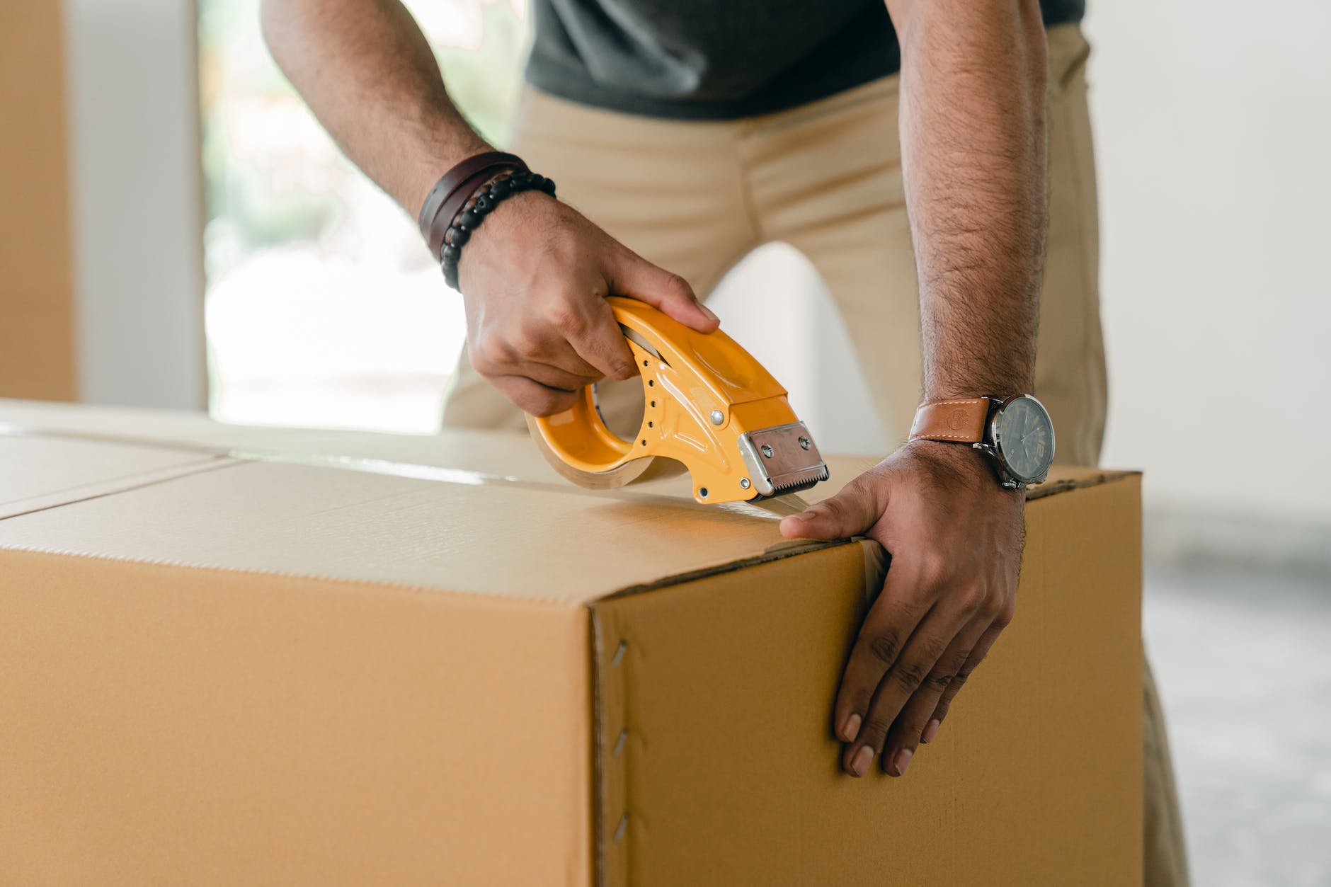 person taping box with yellow tape dispenser