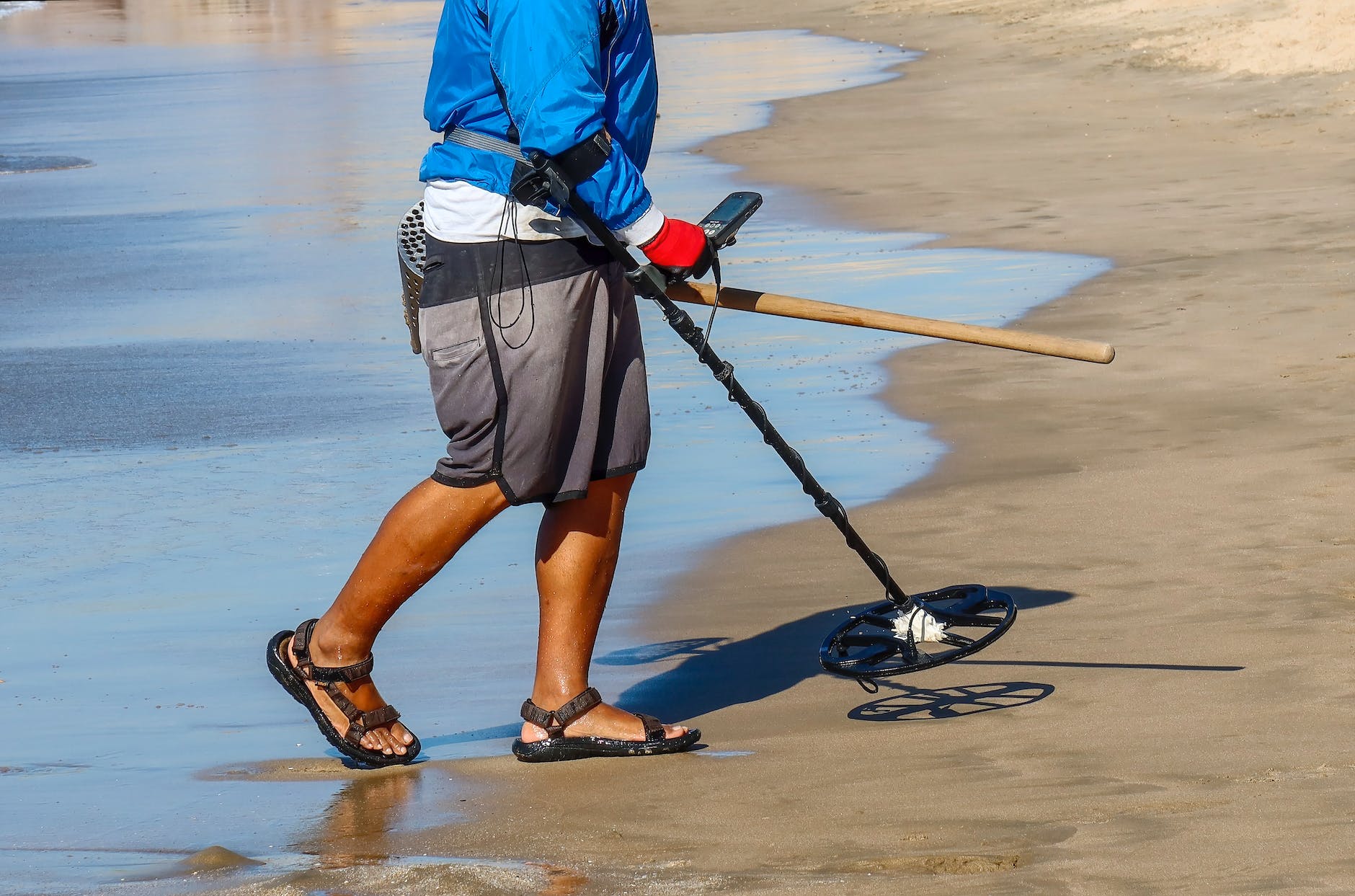 legs of person walking with metal detector on shore