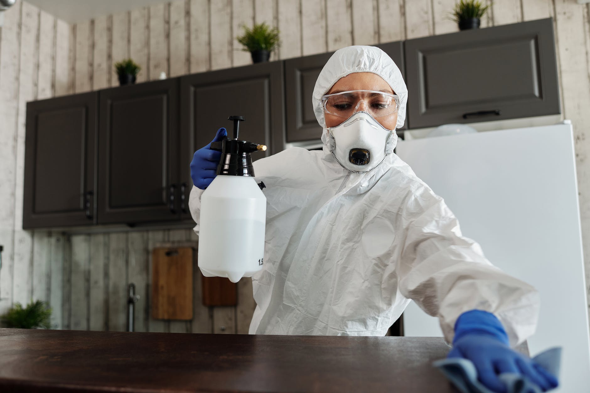 person disinfecting table wearing PPE and respirator