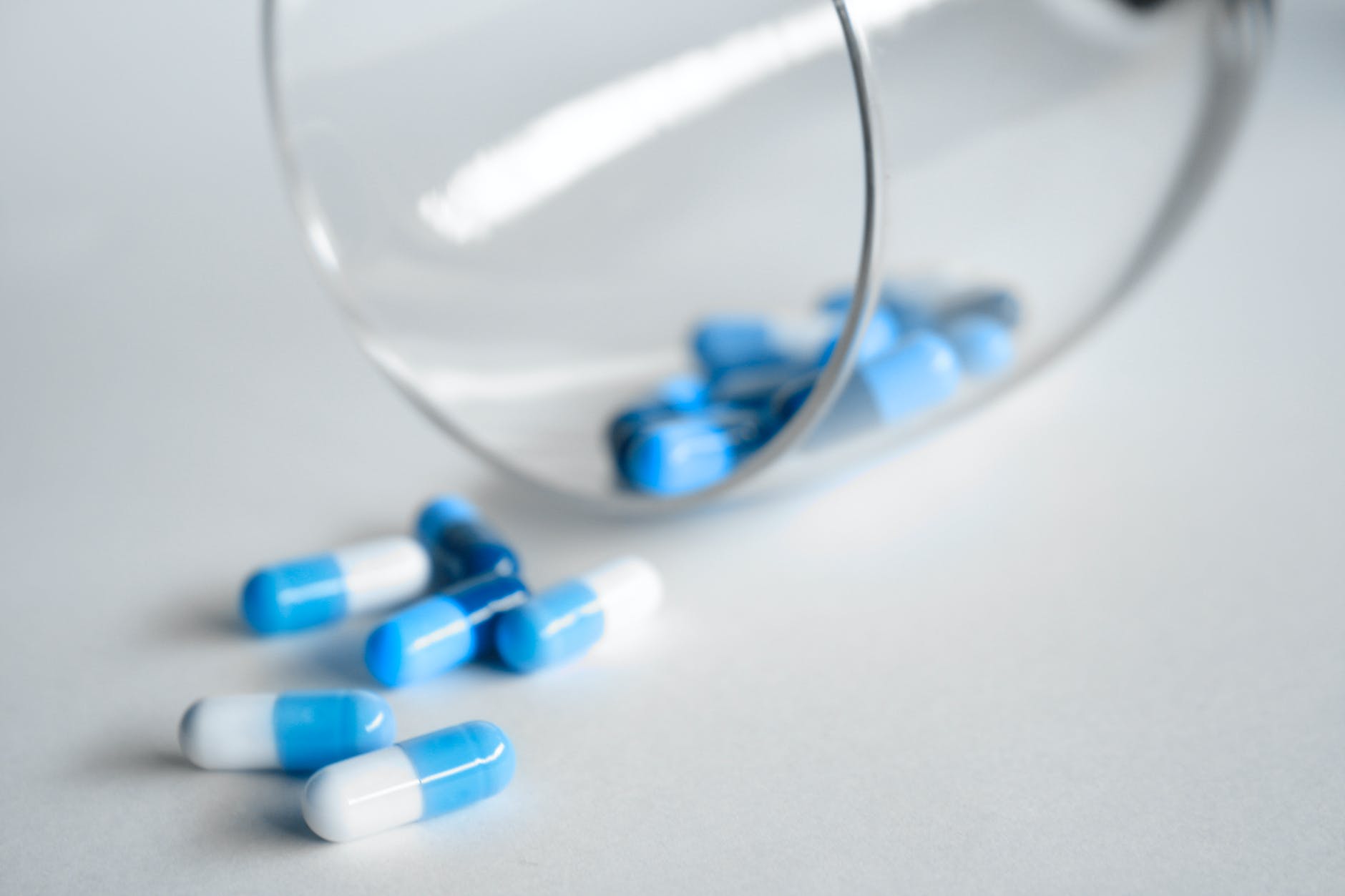 blue and white capsules on white surface next to glass beaker