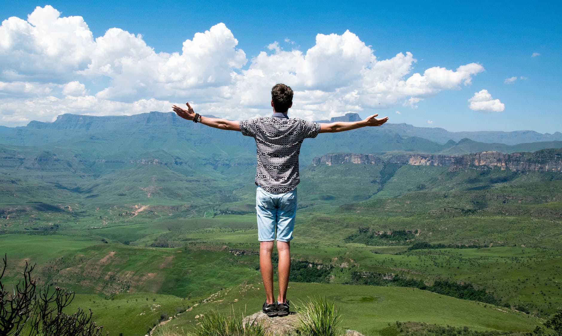 person standing on rock in front facing lush green mountains
