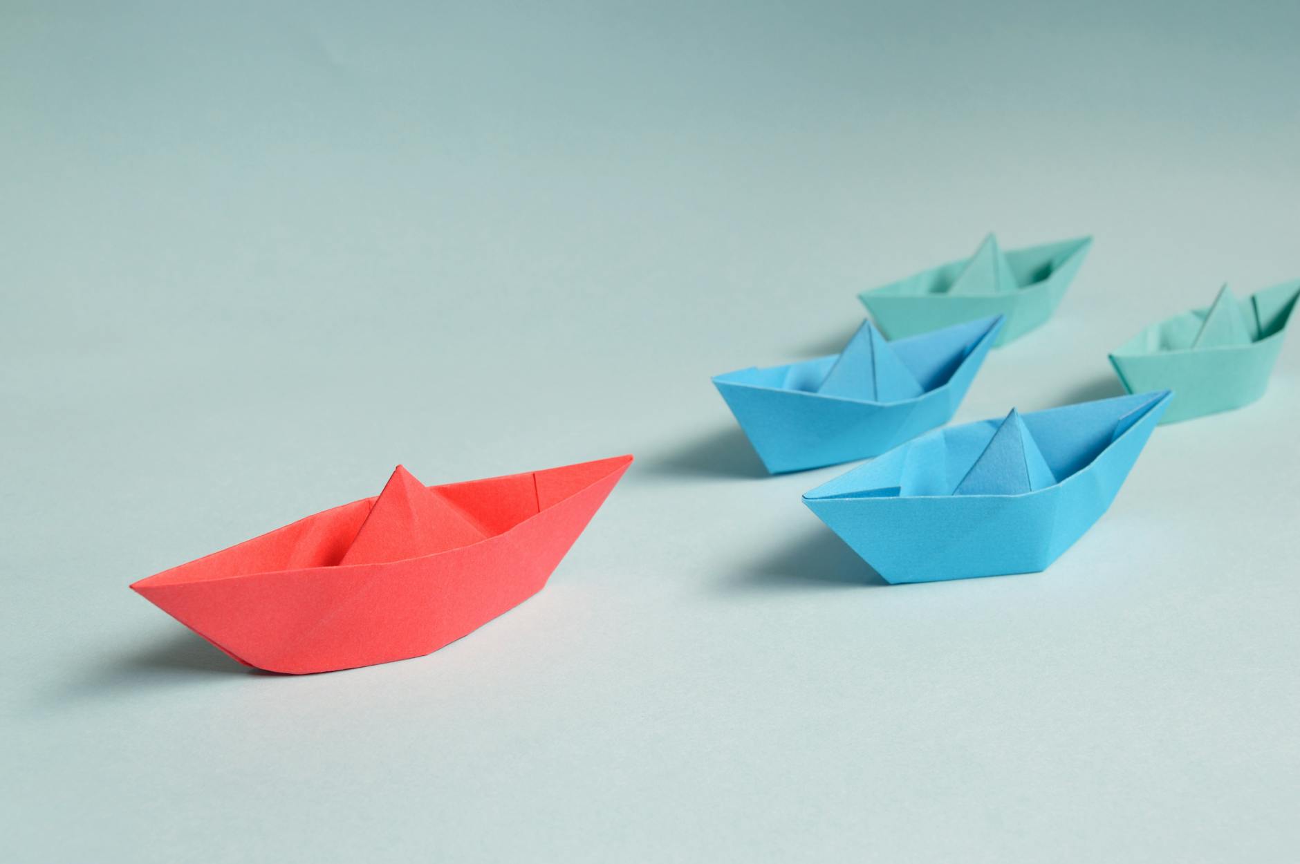 three paper boats: two blue ones behind a red one
